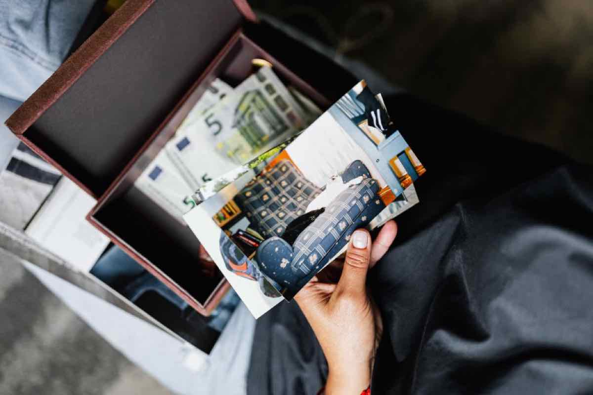 Hand holding an old photograph over a small box containing cash and papers
