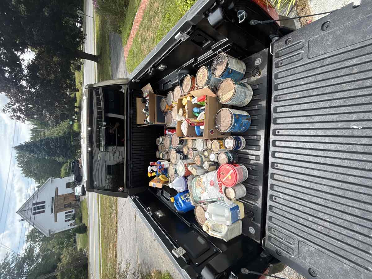 Pickup truck bed full of old paint cans, motor oil, and household chemicals ready for hazardous waste disposal