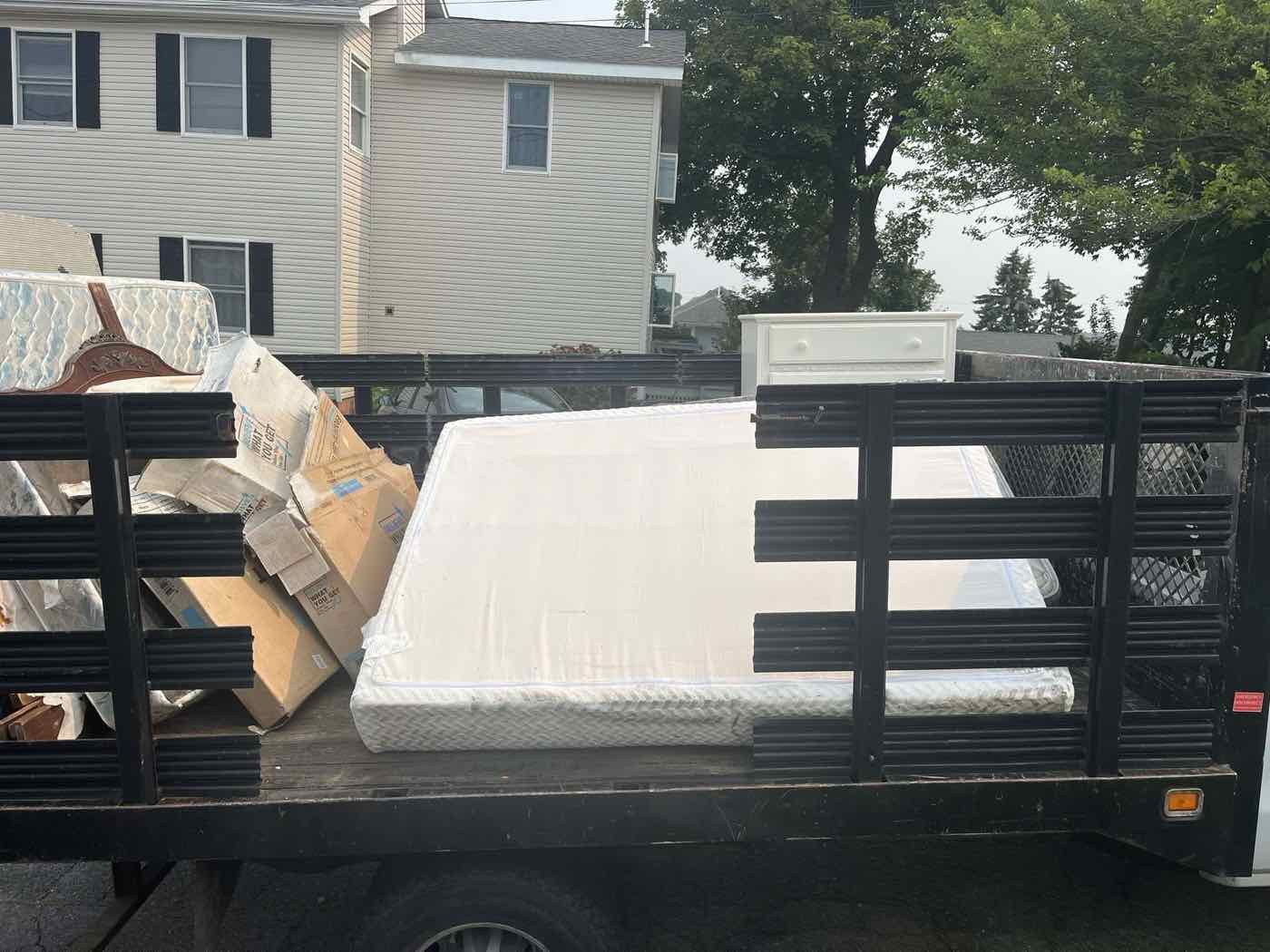 Rear view of a Dumpster Dudes truck loaded with a mattress, dresser, and boxes