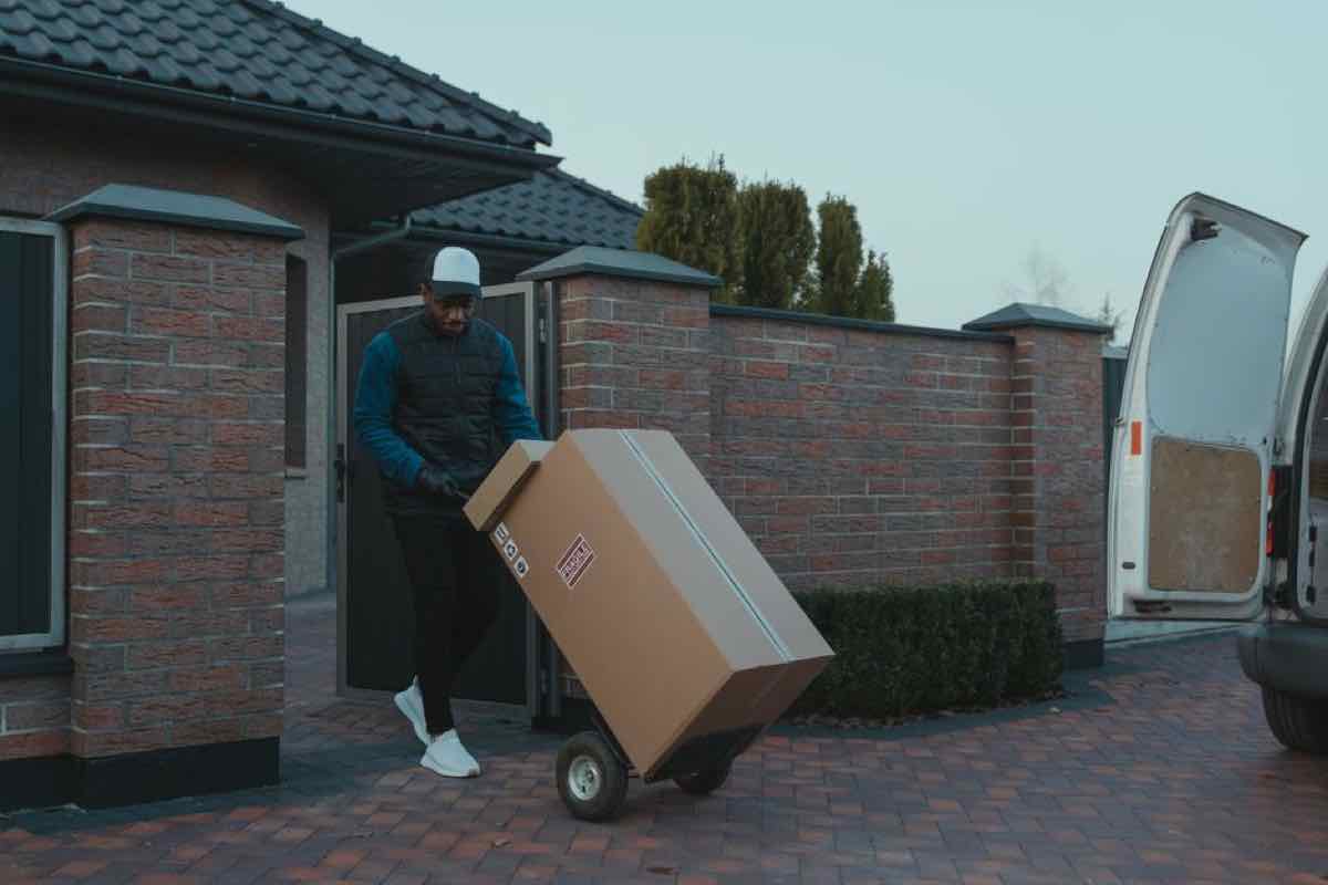 Person loading a large box onto a hand truck next to a moving van in a driveway