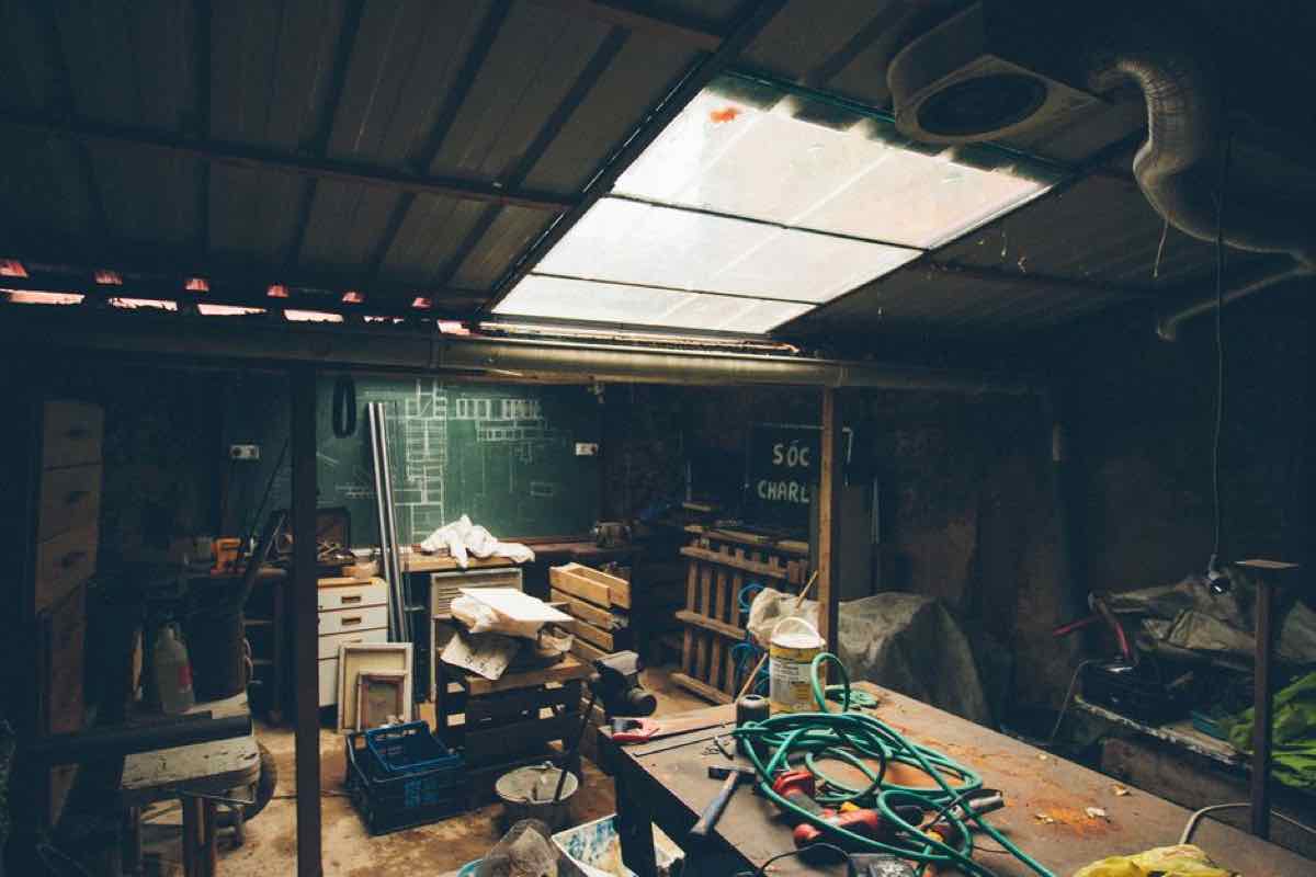Dimly lit, cluttered garage workshop with tools, boxes, and equipment covering every surface