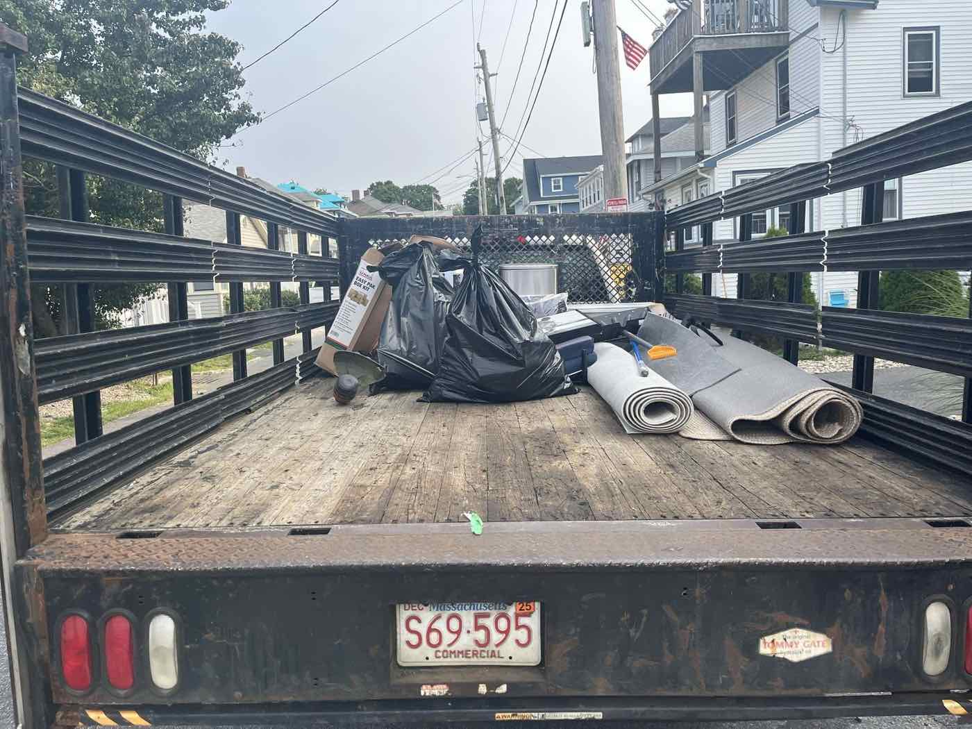 Flatbed truck loaded with junk, boxes, and household items on a South Shore street near Duxbury, MA
